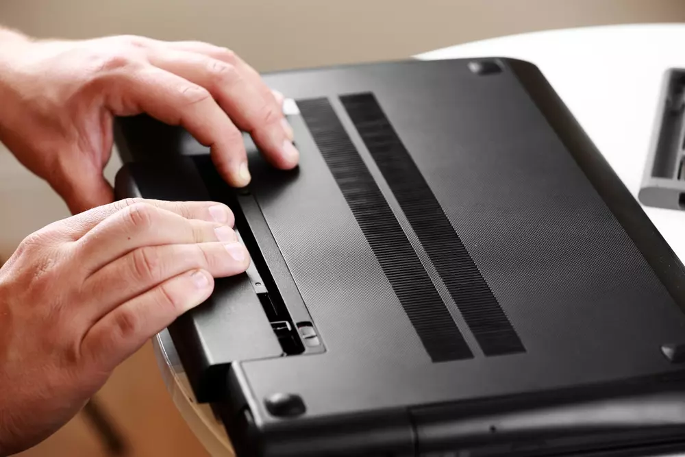 Pessoa trocando a bateria de um notebook.