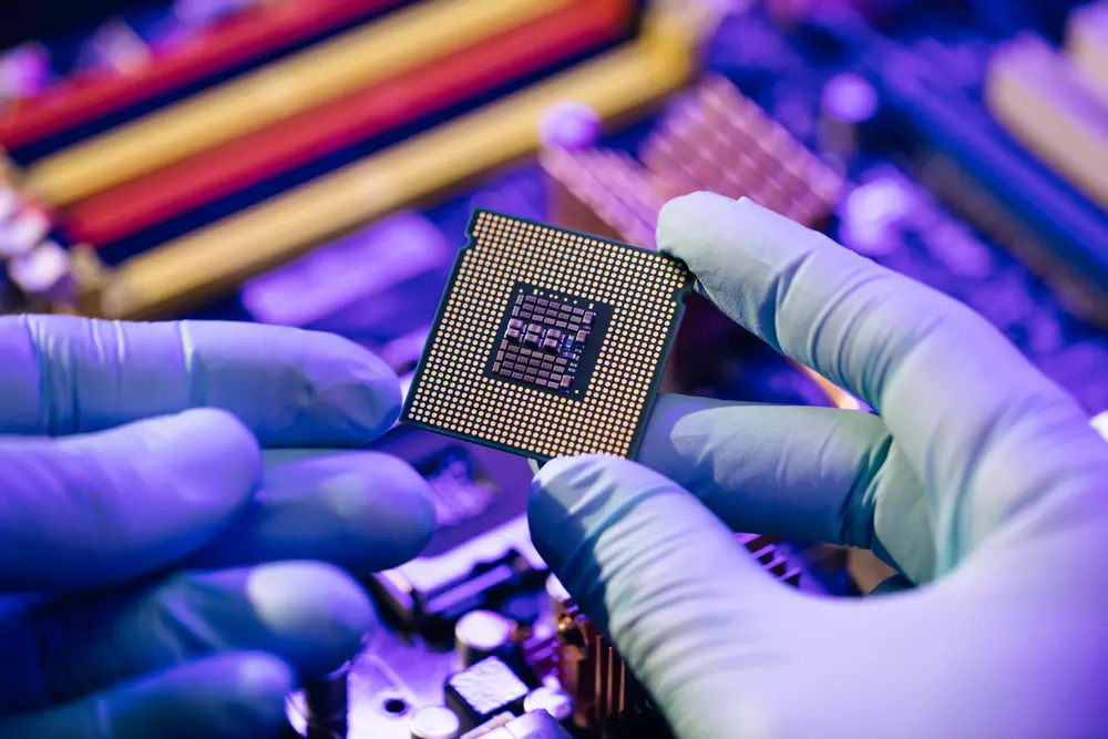 Mãos de uma pessoa segurando um chip de computador com luvas de proteção, destacando detalhes do microchip em uma bancada de eletrônica.