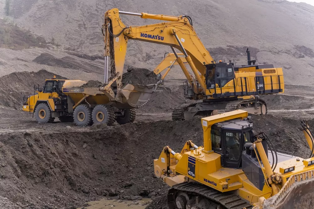 Máquinas pesadas em atividade em uma obra de mineração ou construção, incluindo escavadoras e carregadeiras da marca Komatsu.
