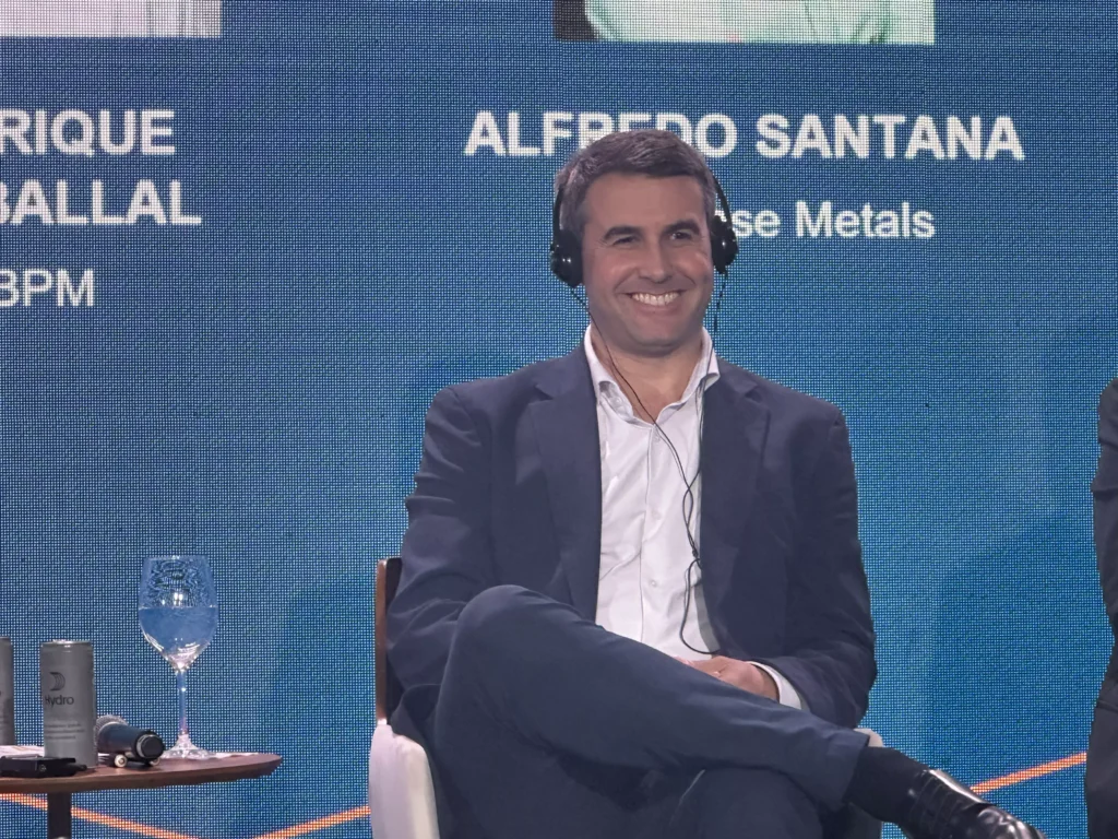 Alfredo Santana, empresário, sorrindo, participando de evento com fundo azul, usando terno e ouvindo fones de ouvido.