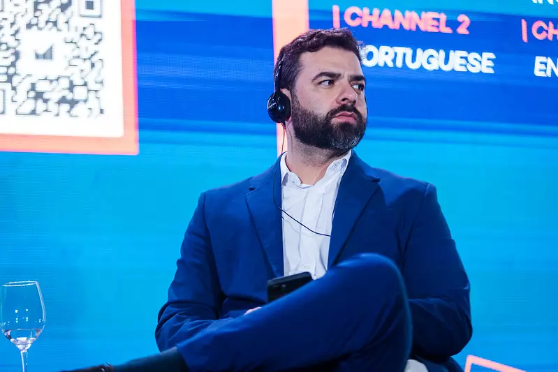 Mauro Barros de terno azul com fone de ouvido, sentado em evento ou entrevista