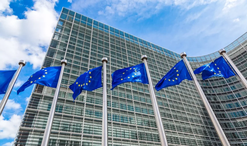Edifício do Parlamento Europeu com várias bandeiras da União Europeia ao vento, simbolizando o pacote legislativo Omnibus da UE que busca simplificar e harmonizar regras
