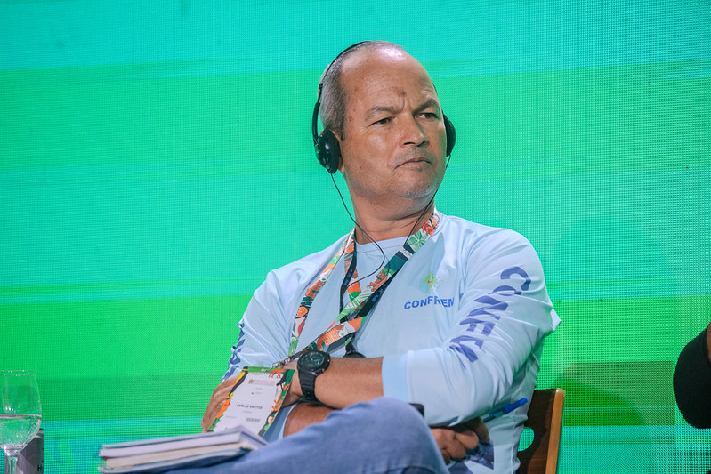 Carlos Alberto Pinto dos Santos em uma conferência, usando fones de ouvido e vestindo uma camisa branca.