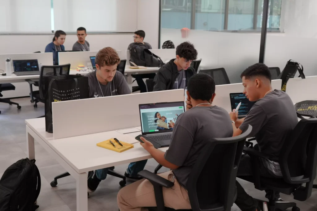 Grupo de pessoas em sala de mineração, usando laptops e tablets para estudos colaborativos em ambiente de tecnologia e inovação.