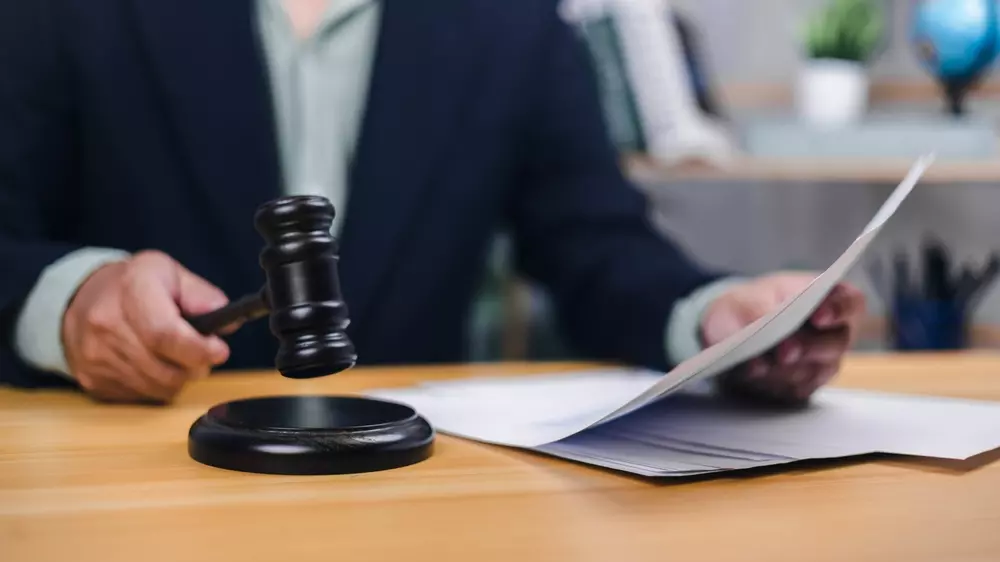 Pessoa segurando martelo de juiz, simbolizando regulação, segurança e aspectos legais no Brasil com documentos na mesa