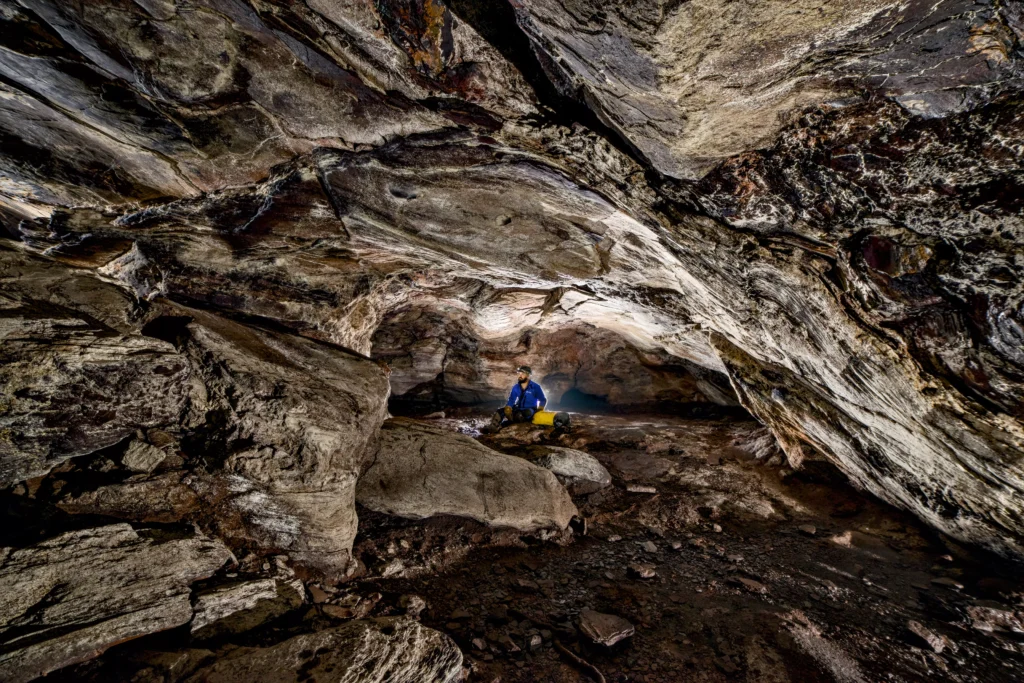 Explorador dentro de uma cavidade natural de rochas, mostrando a grandiosidade da formação geológica, ideal para aventuras de exploração e turismo de cavernas.