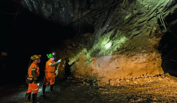 Equipe de mineração da AngloGold explorando uma caverna subterrânea com equipamentos de segurança e luzes