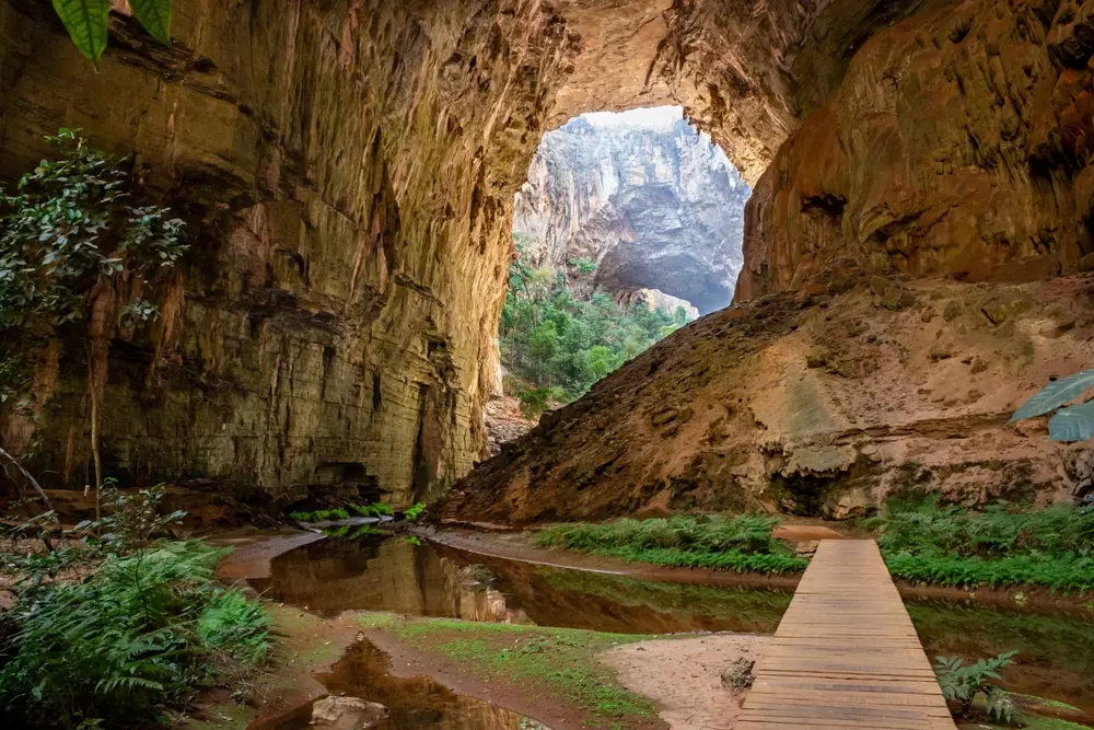 Interior das cavernas no Parque Nacional Cavernas do Peruaçu, com uma ponte de madeira, vegetação exuberante e formações rochosas impressionantes.