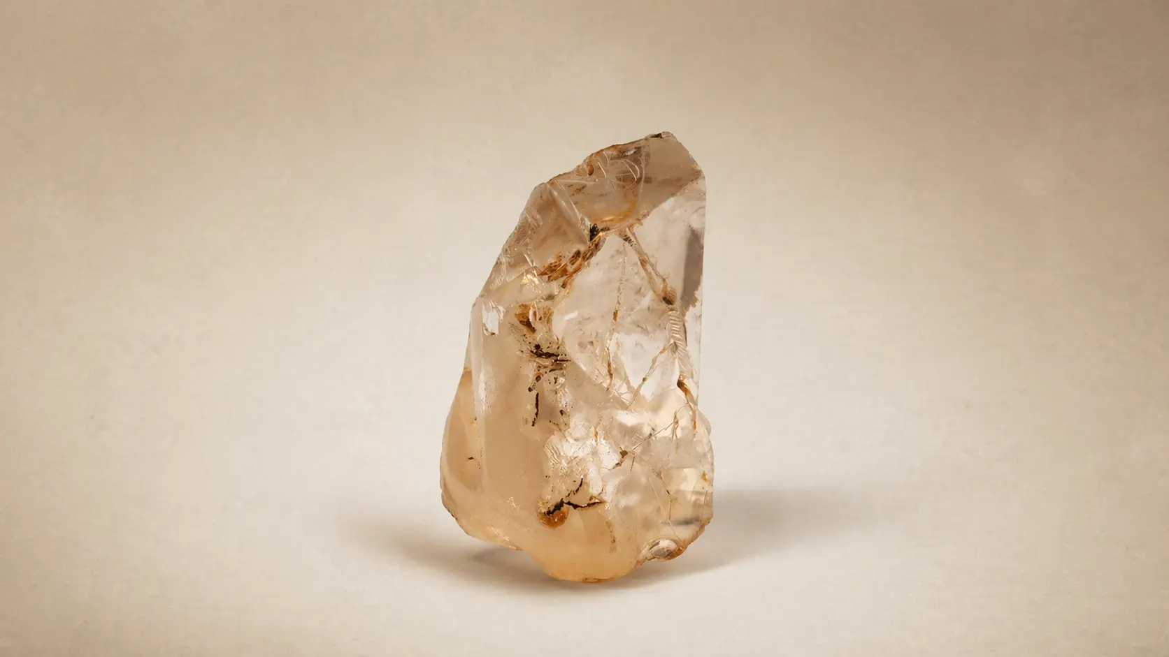 Grande diamante bruto do século XVIII com tons de âmbar e inclusões internas, posicionado verticalmente sob fundo neutro.