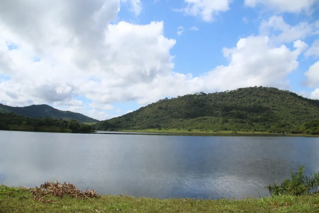 Lago formado na antiga cava de exploração mineral na Serra Pelada, inundada pela chuva e lençol freático, com vista para montanhas verdes sob céu parcialmente nublado.